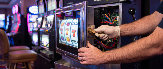 Naklejka premium Technician opening electronic slot machine panel on bright casino