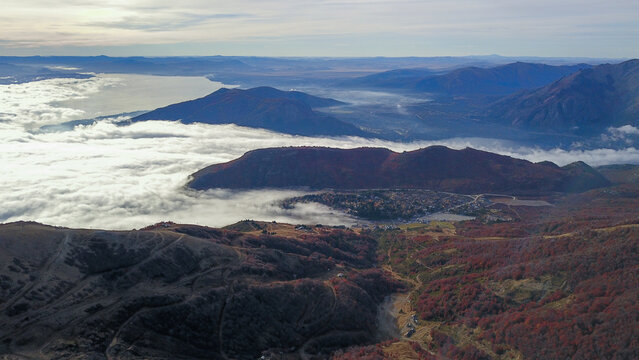 Aerial view of the mountainous landscape featuring autumn foliage, dense cloud cover over the valley, and distant lakes in San Carlos de Bariloche, Rio Negro Province, Argentina.