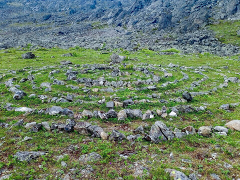 Stone labyrinth on the alpine meadow with green grass among rocks