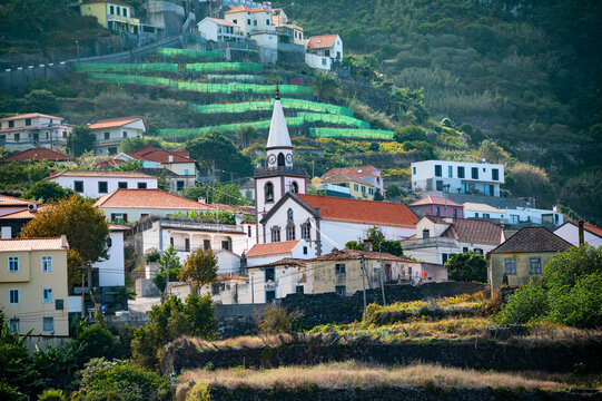 Scenic view of a traditional rural village with a white church and terraced green agriculture on the mountainous island of Madeira