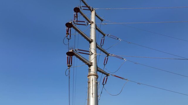 High voltage transmission tower with insulators and overhead power lines against clear blue sky