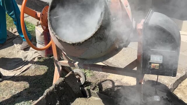 Horizontal video: a concrete mixer working on a construction site, cement being poured inside, light dust and haze visible from dry material, industrial atmosphere.