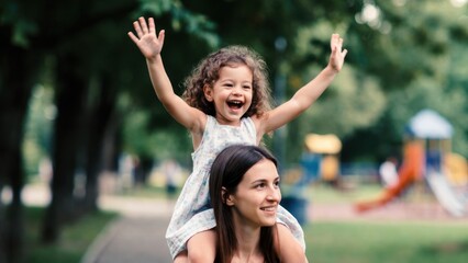 Fototapeta premium Mother carrying daughter on shoulders in playground park