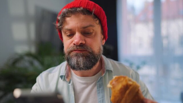 A man enjoying a fresh croissant for breakfast and using his smartphone