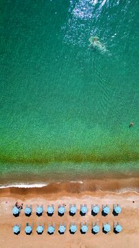 Top-down view of sandy beach with sun umbrellas and turquoise sea water
