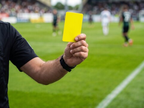 Soccer referee showing yellow card on football field