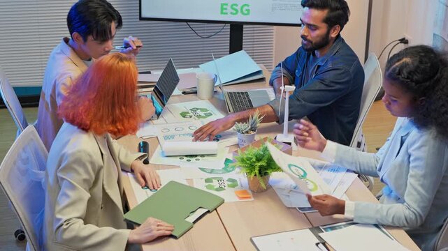 Diverse multiracial business team sitting in night office presenting ESG restructuring plan for clean energy profit growth, corporate consulting analysts strategy meeting concept