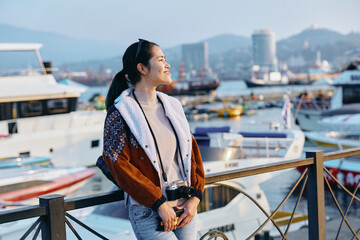 Woman standing by a harbor with boats in the background, wearing a stylish fleece and warm coat, enjoying a sunny day by the water, leisure travel mood, candid moment, seaside scenery and urban © SHOTPRIME STUDIO