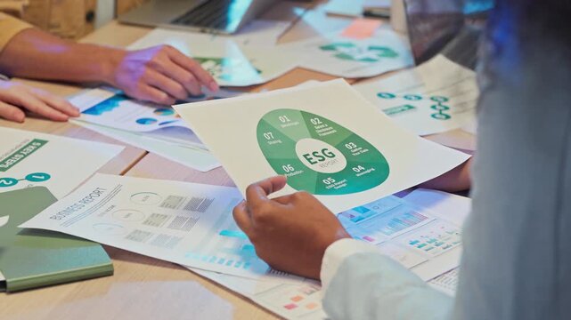 Close up diverse hands holding ESG analysis documents with charts and graphs, multiracial business analysts reviewing clean energy restructuring report, corporate consulting strategy concept