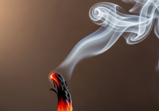 Close-up of an Extinguished Candle Wick with Glowing Red Embers and Elegant White Smoke Wisps on Brown Background