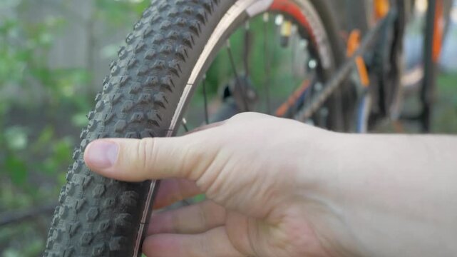 Spinning bicycle tire is touched by hand, feeling rubber's knobby texture. Tire's tread is important for maintaining control on various terrains. Repairs bicycle upside down outdoor, small business