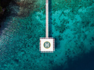 Obraz premium Aerial view of helipad over the sea. Helicopter parking platform station linked to the land by long concrete bridge over turquoise water of Andaman sea at Nyaung Oo Phee island in Burma or Myanmar.