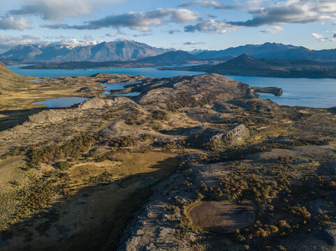 Aerial view of rugged landscape with glacial lakes, rolling hills, and distant mountains under a cloudy sky in San Carlos de Bariloche, Rio Negro Province, Argentina.