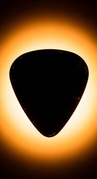 Silhouette of a black guitar pick glowing with warm orange light background