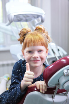 little girl at dentist's appointment. Girl is sitting in dental chair and giving thumbs-up. Child has great mood in dental office