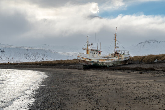 Abandoned fishing boat stranded on beach in Iceland with snowy mountains