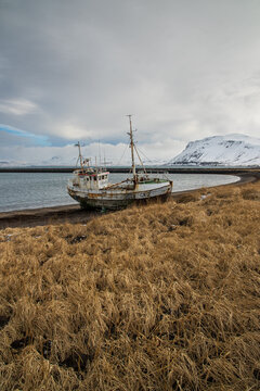 Old fishing boat beached in Icelandic fjord with mountains