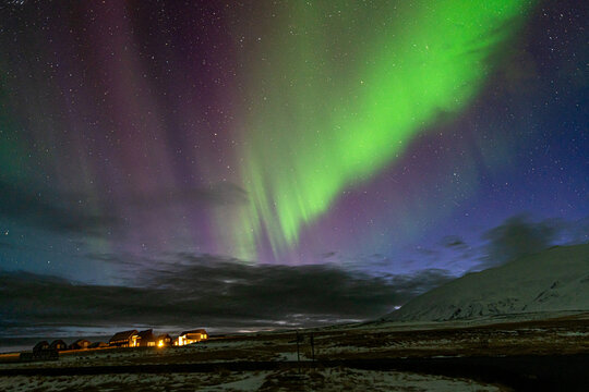 Green and purple aurora over illuminated houses in snowy Icelandic landscape