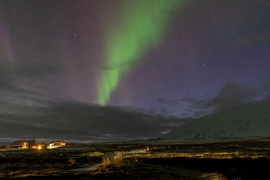 Vibrant green northern lights aurora borealis over a snowy rural landscape with cozy illuminated houses, Iceland