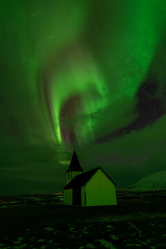 Vertical northern lights over church and snowy landscape in Iceland