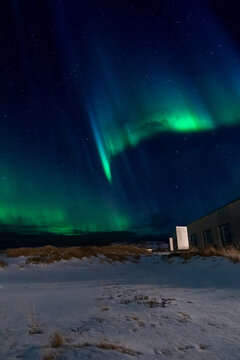 Vertical view of northern lights above snowy cabin in Iceland
