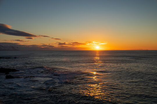 Golden sunset over the ocean with sun reflection on water surface and dramatic clouds, Iceland