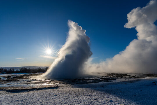 Strokkur geyser eruption with water splash and steam under a bright winter sun, Golden Circle, Iceland