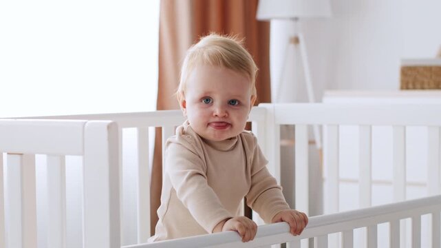 Smiling Baby Boy With Blue Eyes Standing In Crib, Enjoying Playtime At Home, Surrounded By Soft Toys In Nursery. Indoor Setting Focusing On Early Childhood Development Concept.