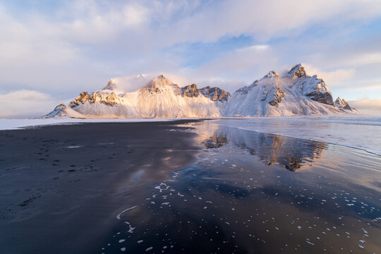 Vestrahorn mountain reflected in shallow water on black sand beach, Iceland