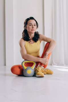 Fit woman resting on floor beside kettlebell in bright fitness studio after training session