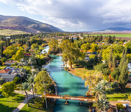 Aerial view of the Asi River flowing through the lush greenery of Nir David, featuring a pedestrian bridge and palm trees in Nir David, North District, Israel.