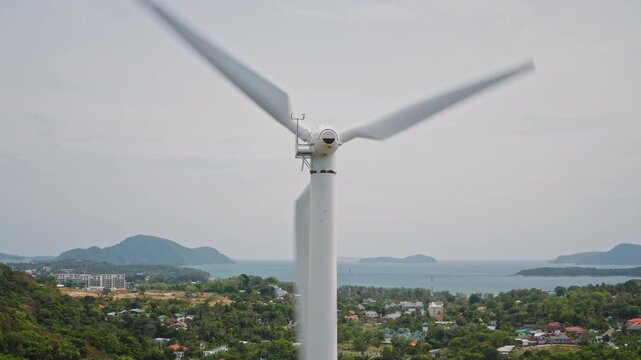 Wind turbine blades spinning, creating renewable electricity above a lush, green coastal landscape with the ocean and islands visible in the background, representing sustainable power for Thailand