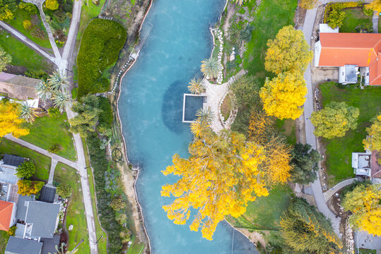 Aerial view of the Asi River flowing through the lush greenery and vibrant yellow trees of Nir David, North District, Israel.