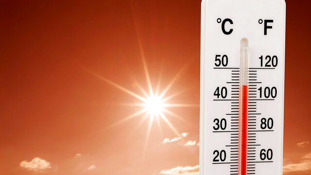Outdoor thermometer showing high temperature of fifty degrees celsius and one hundred twenty degrees fahrenheit against bright sun in orange sky for heatwave and summer heat concept.