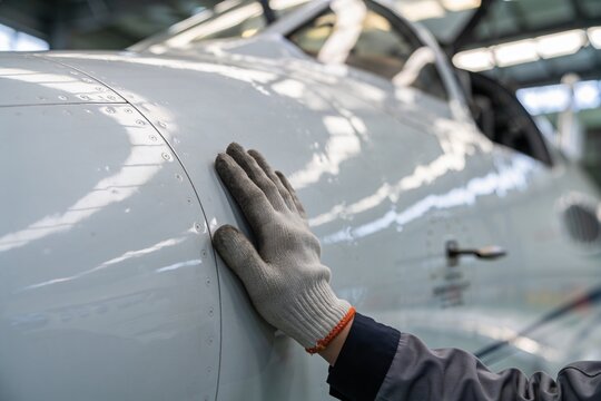 A close-up view of a gloved hand resting on the polished white exterior fuselage of an aircraft.