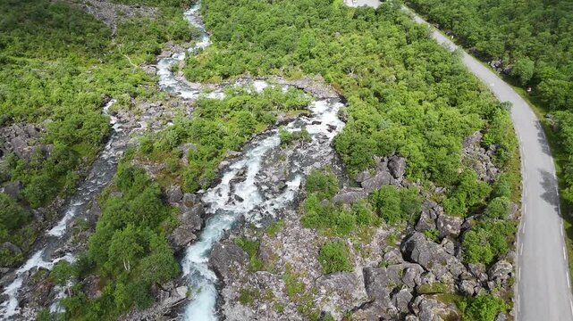 Aerial drone pan up of lower Trollstigen with flowing river and tree covered mountain walls, Norway