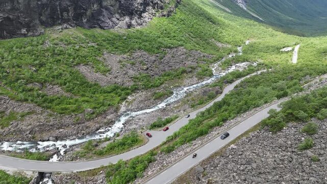 Aerial drone pan up of lower Trollstigen with flowing river and tree covered mountain walls, Norway