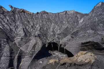 Rugged volcanic landscape with dark rock formations and a deep crater under clear blue sky,ICELAND © SHUNJI ZHOU
