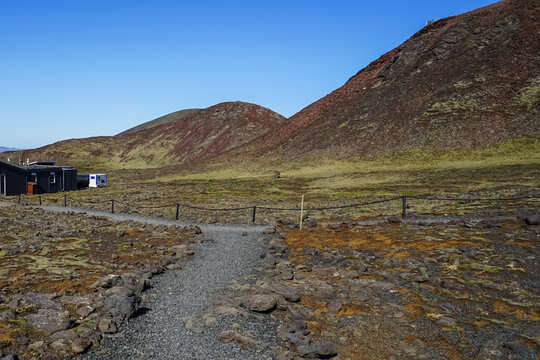 A gravel path winds through a barren, rocky landscape with rolling hills under a clear blue sky,ICELAND