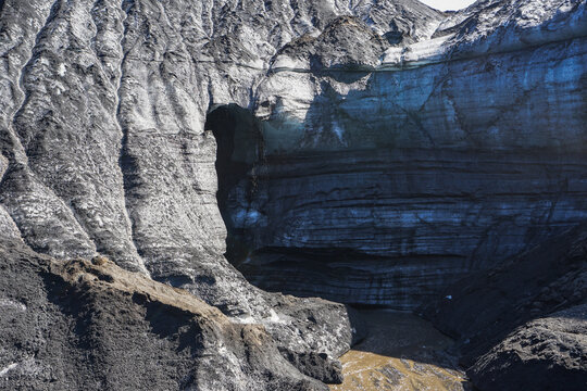 Rugged rock formation with a natural arch and layered sedimentary structure in a dry, mountainous environment,Katla Ice Cave,ICELAND