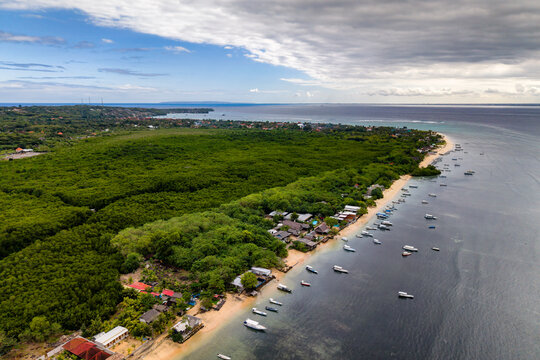 Flying over a lush tropical island beach lined with boats and dense green forest