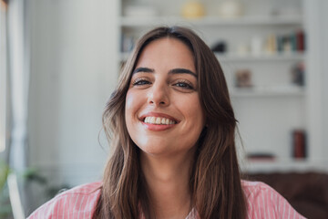 Fototapeta premium Happy young woman smiling broadly and looking directly at the camera, conveying joy and well-being while relaxing in a casual home setting
