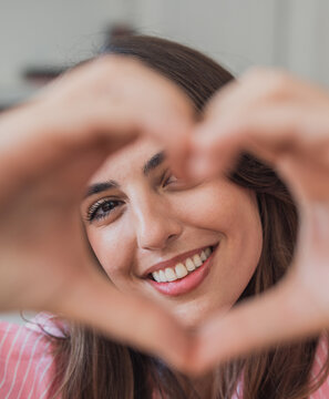 Young woman smiling while forming a heart shape with her fingers, expressing love, affection, and happiness through a positive gesture