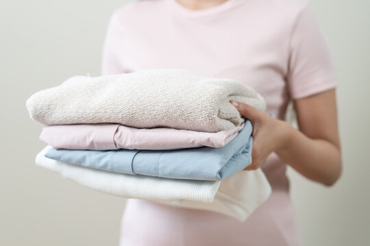 Close up of a woman holding a stack of clean folded clothes.