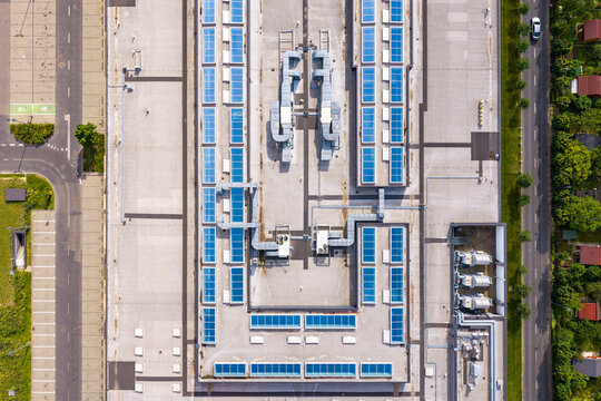 Aerial view of shopping center rooftop featuring rows of solar panels and industrial HVAC units surrounded by parking areas and roads in Warsaw, Masovian Voivodeship, Poland.