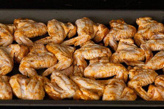 Raw chicken wings seasoned with spices arranged neatly on a baking tray ready for cooking in a kitchen setting with dark background