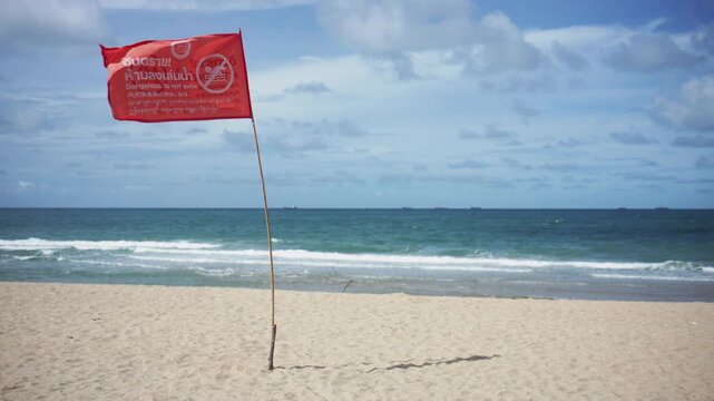 4K  Red warning flag on sandy beach with blurry sea background