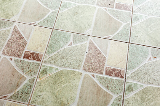 Close-up of vintage-style ceramic tile floor with irregular geometric pattern in muted green, beige, and terracotta tones