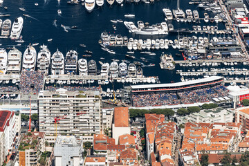 Fototapeta premium Monaco city center and Port Hercules during the Formula One Grand Prix with grandstands, luxury yachts and spectators viewed from Tete de Chien