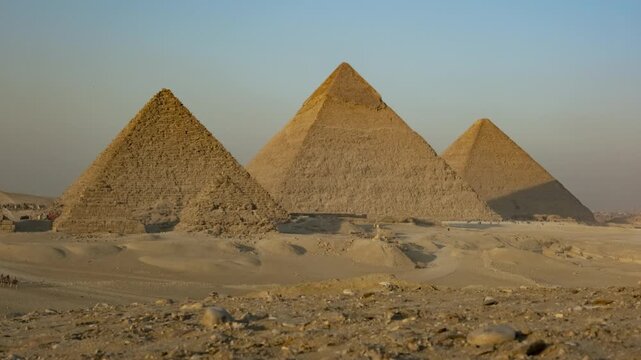 Timelapse zooming out of three Great ancient Egyptian pyramids against background blue sky at Giza plateau near Cairo, Egypt, evening falls